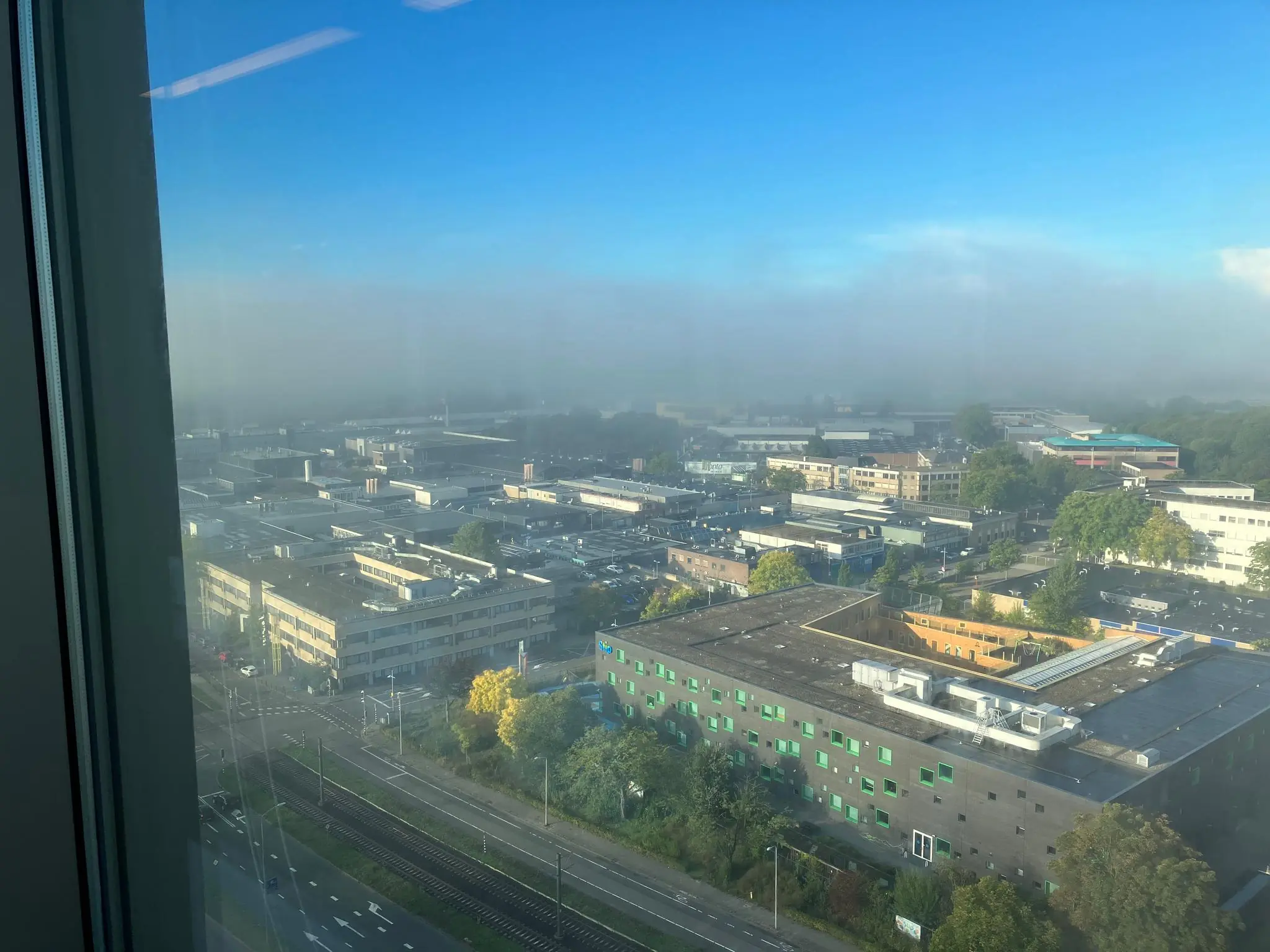 Uitzicht vanuit een hoog gebouw op industrieterrein Vliegend Hertlaan in Utrecht met ochtendmist en blauwe lucht.